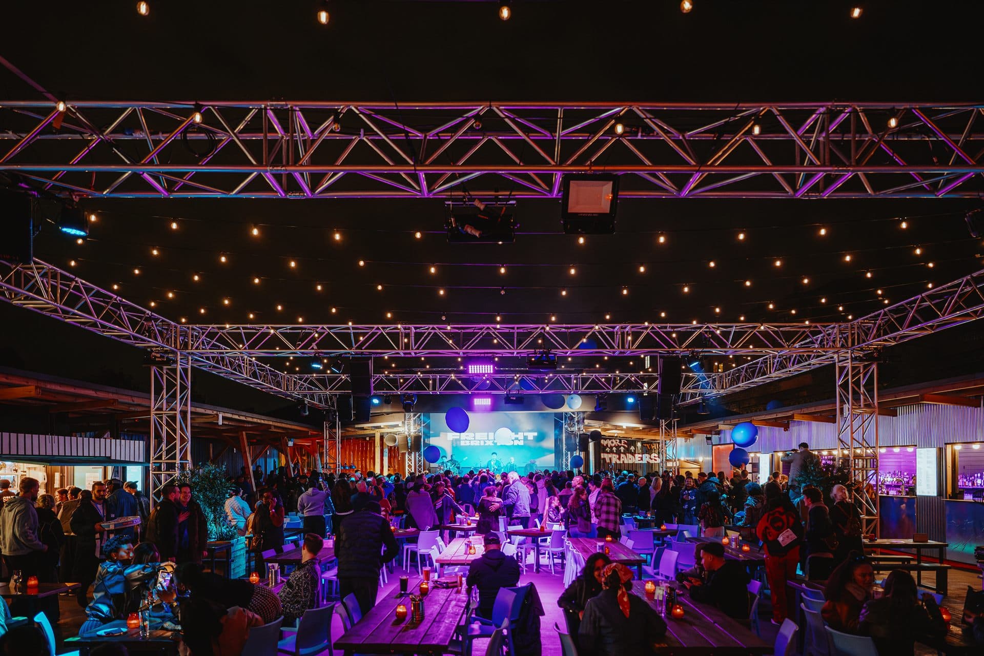 Freight Brixton at night, lit in purple with the crowd at long tables
